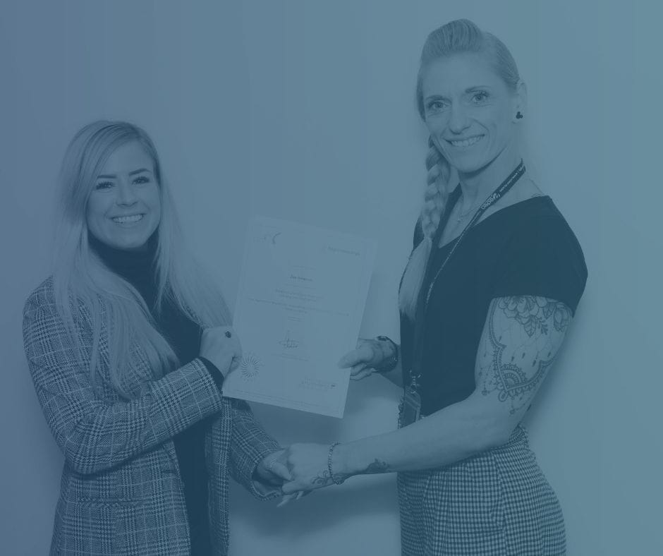 Two female colleagues with one handing a certificate to the other.