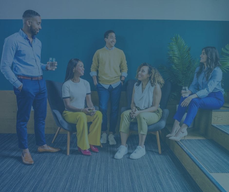 A group of colleagues sitting in a lounge area discussing topics.