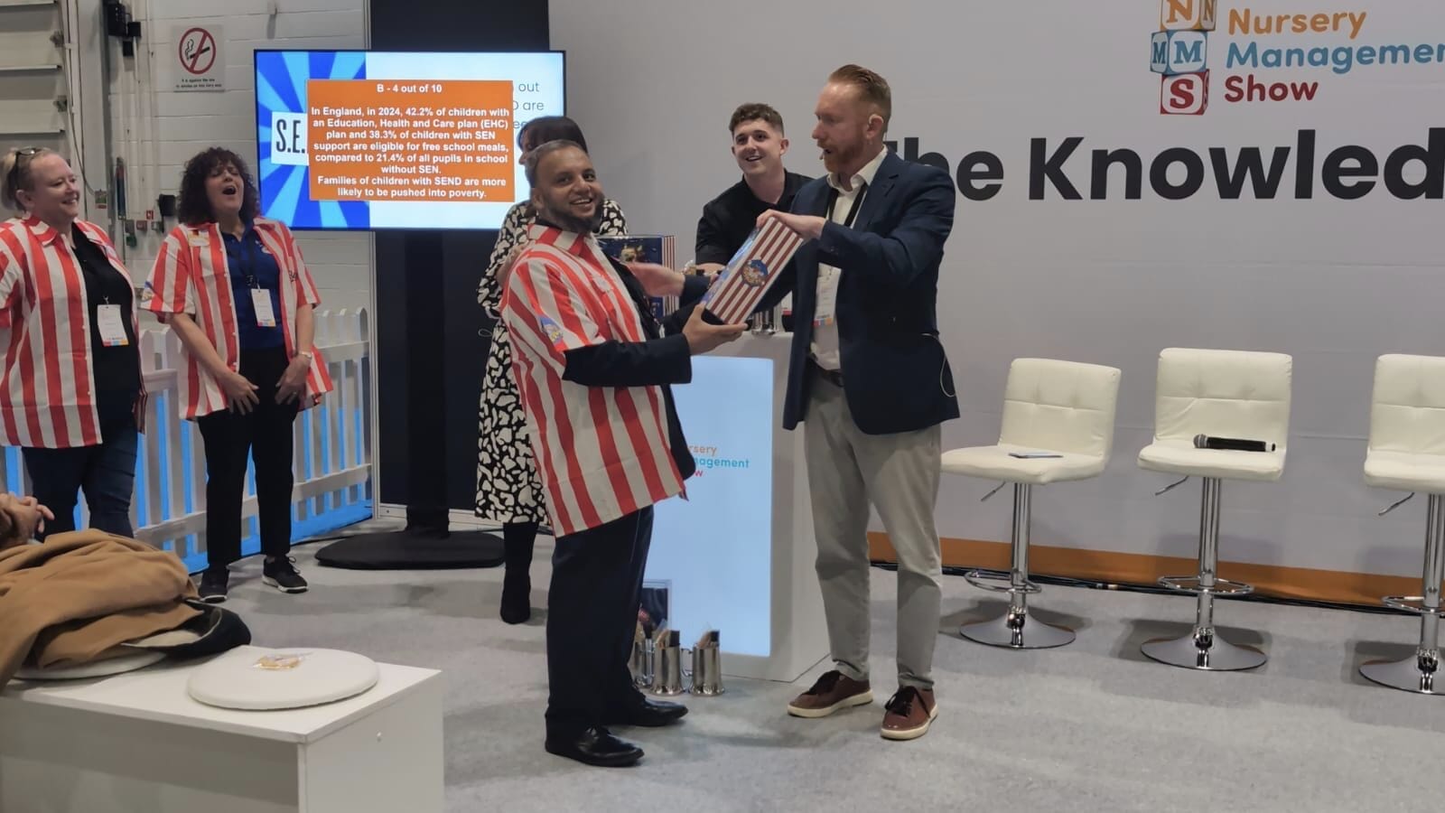 Gameshow contestant (wearing red stripey shirt) receiving prize following participation in Eden Plays Bullseye. The text Knowledge hub reads on the back wall.